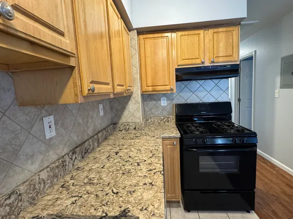 a kitchen with granite countertop a stove top oven cabinetry a chimney and a large window