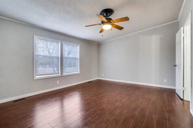 an empty room with wooden floor chandelier fan and windows