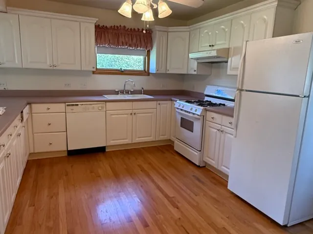 a kitchen with stainless steel appliances granite countertop a refrigerator a stove a sink and white cabinets with wooden floor