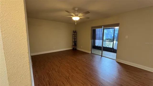 a view of an empty room with wooden floor and a ceiling fan