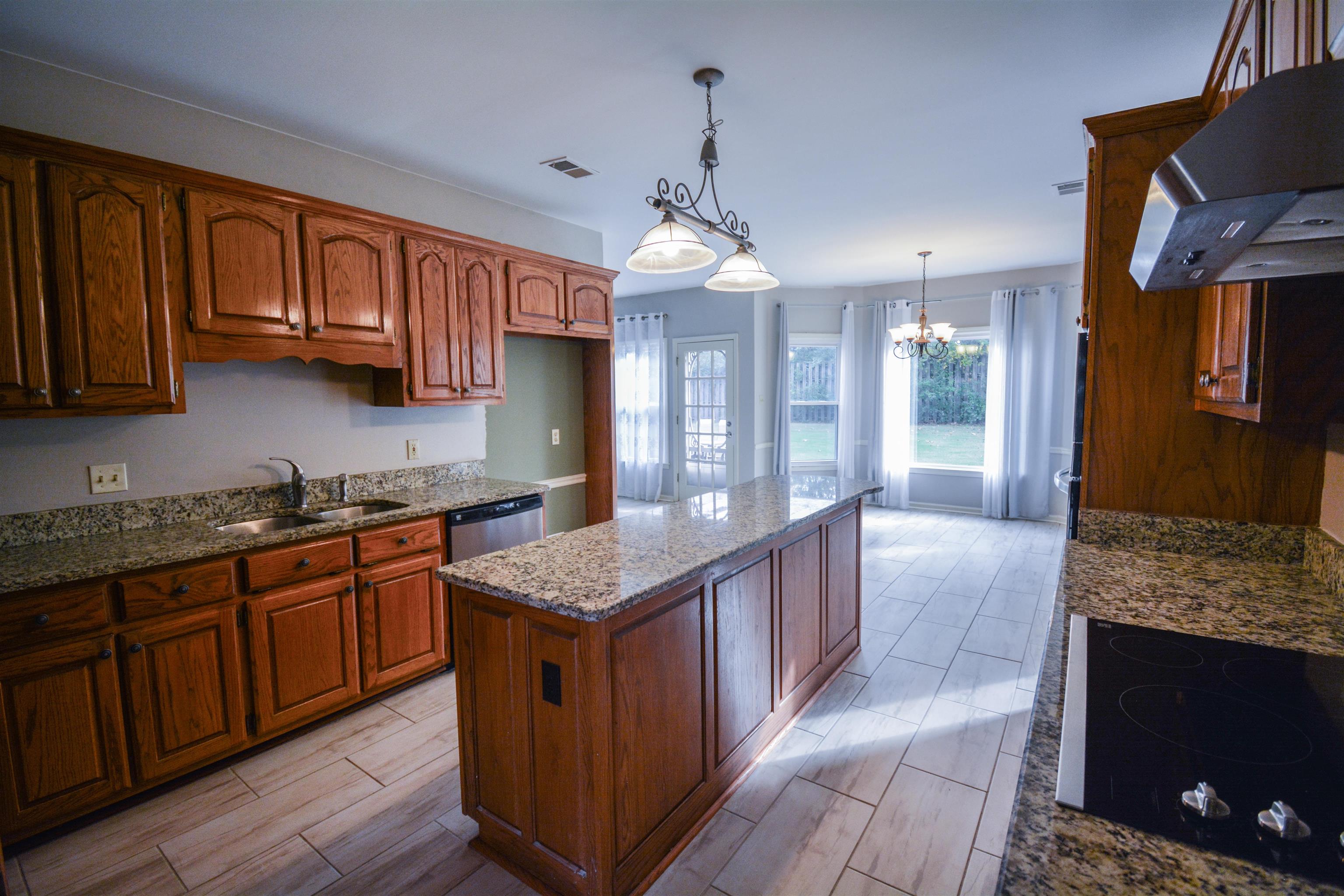 745 Roehampton Court Collierville, TN 38017 - Photo 5 of 40 Kitchen featuring dark stone countertops, black electric stovetop, under cabinet range hood, hanging light fixtures, and a kitchen island