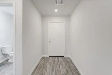 a view of a hallway with wooden floor and a toilet