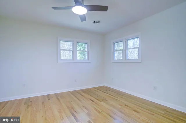 an empty room with wooden floor chandelier fan and windows