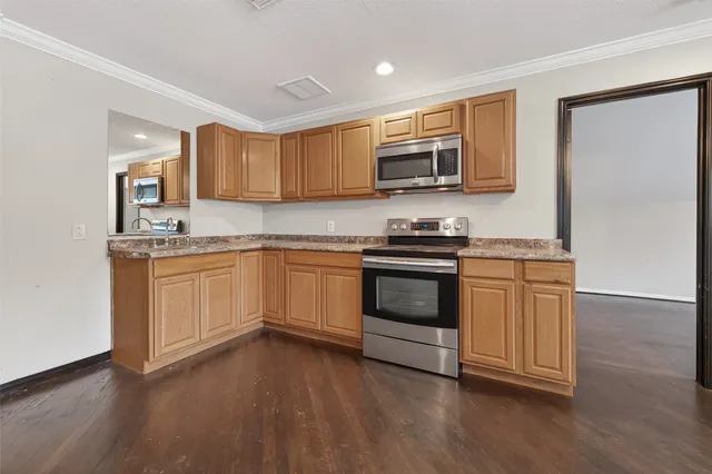 a kitchen with stainless steel appliances granite countertop white cabinets a sink a stove a microwave and wooden floors
