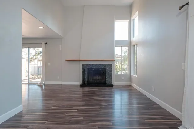 a view of an empty room with wooden floor fireplace and a window