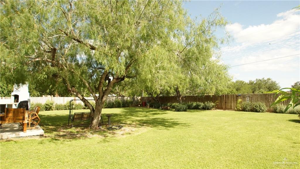 414 Ric Mar Street Edinburg, TX 78541 - Photo 6 of 36 Expansive backyard featuring mature trees, a privacy fence, a built-in outdoor fireplace, and a concrete patio