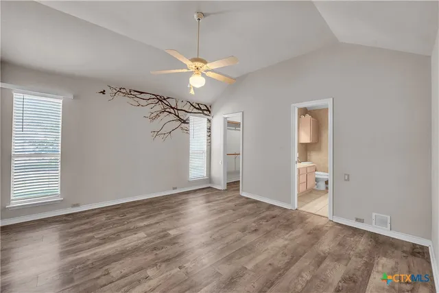 an empty room with wooden floor fan and windows