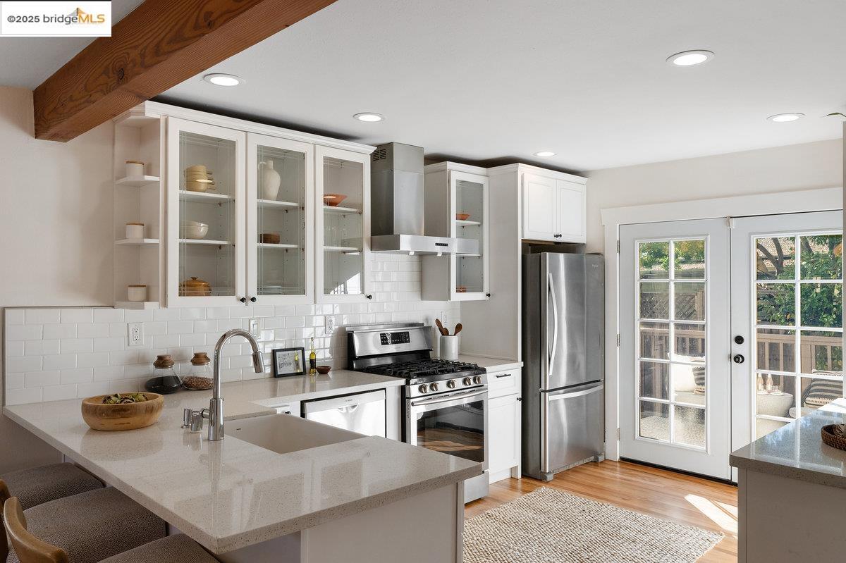 3056 California Street Oakland, CA 94602 - Photo 15 of 44 Kitchen featuring appliances with stainless steel finishes, light stone countertops, decorative backsplash, wall chimney range hood, and white cabinets
