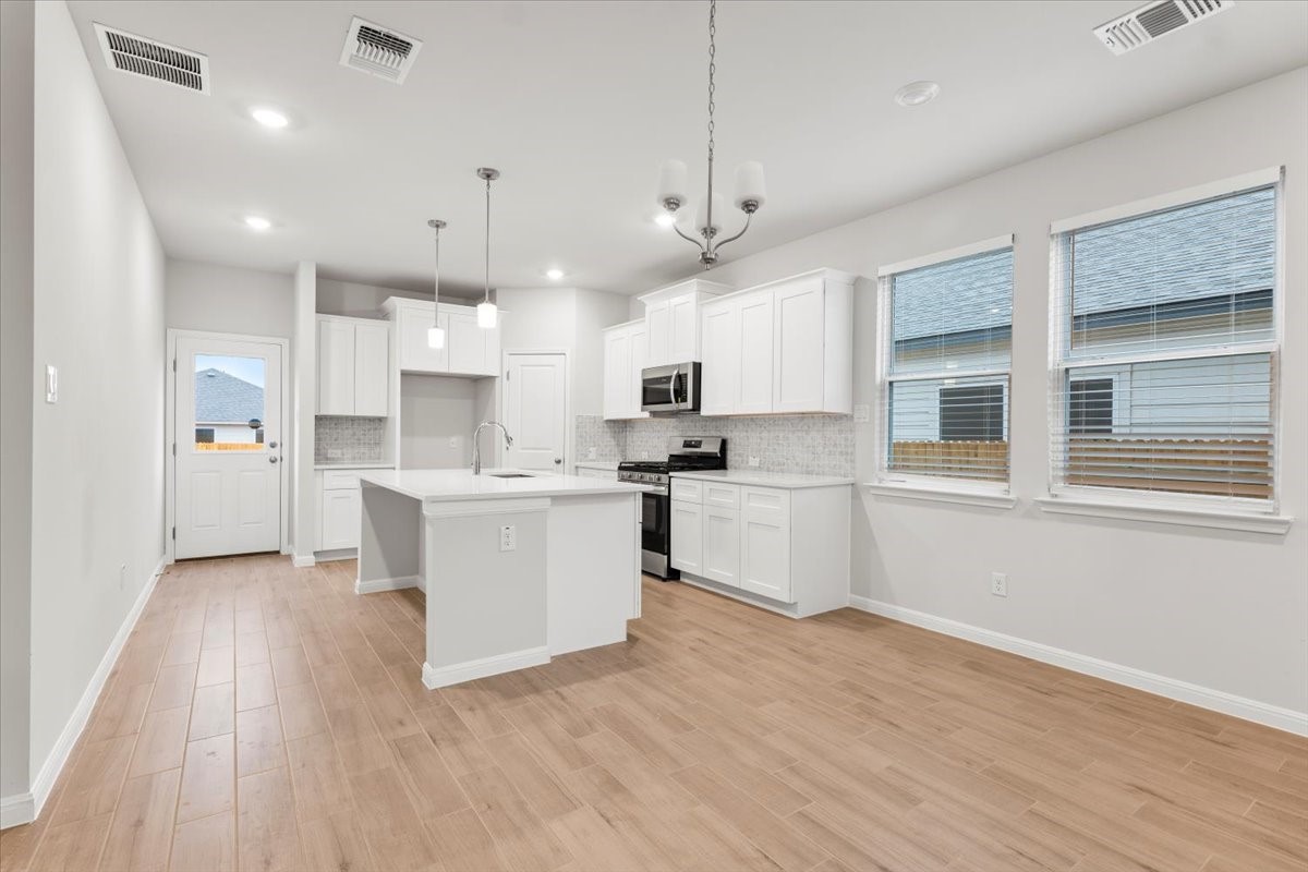 320 Windstar Road Liberty Hill, TX 78642 - Photo 7 of 29 a kitchen with stainless steel appliances kitchen island a refrigerator a sink dishwasher a stove and white cabinets with wooden floor