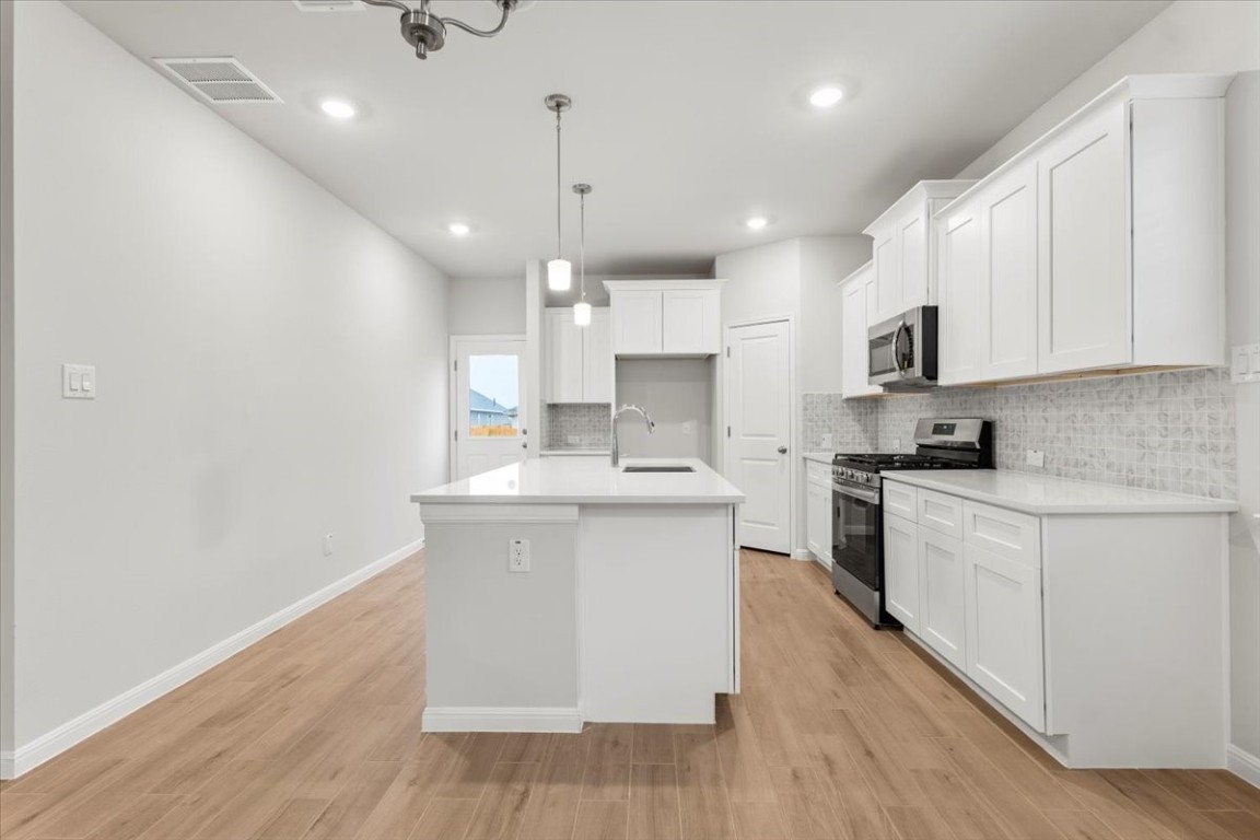 320 Windstar Road Liberty Hill, TX 78642 - Photo 8 of 29 a kitchen with stainless steel appliances granite countertop a sink a stove a refrigerator and white cabinets with wooden floor