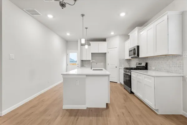 a kitchen with stainless steel appliances granite countertop a sink a stove a refrigerator and white cabinets with wooden floor