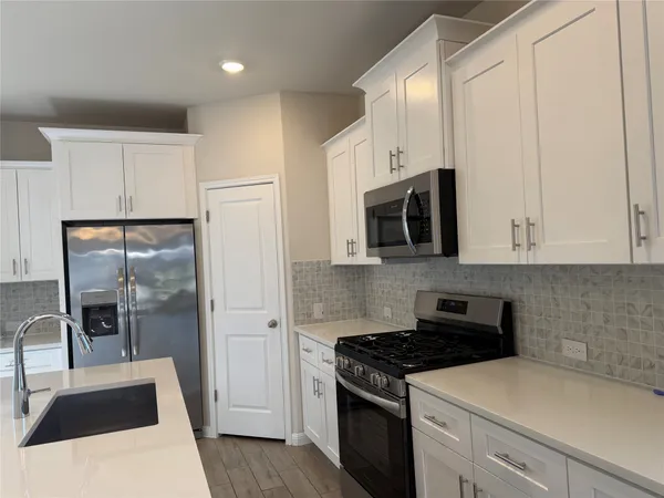 a kitchen with stainless steel appliances granite countertop a sink a stove a refrigerator and white cabinets with wooden floor