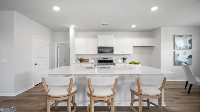 a kitchen with stainless steel appliances kitchen island granite countertop a dining table chairs and a refrigerator