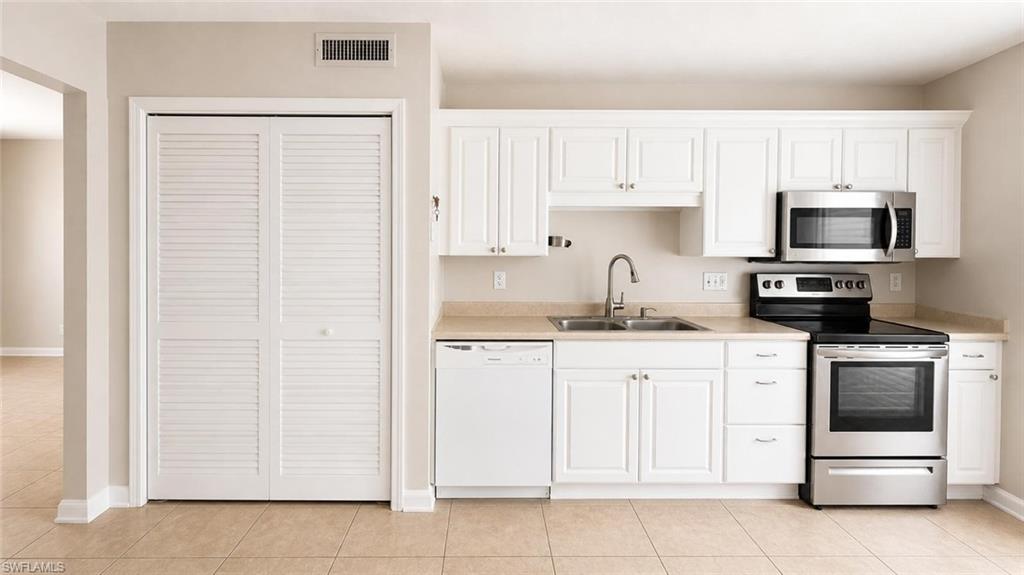 5410 16th Place Southwest, Unit B1 Naples, FL 34116 - Photo 9 of 26 a kitchen with white cabinets and stainless steel appliances