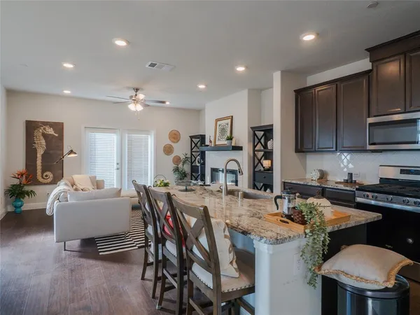a kitchen with stainless steel appliances granite countertop a stove a refrigerator a kitchen island a dining table and chairs with wooden floor