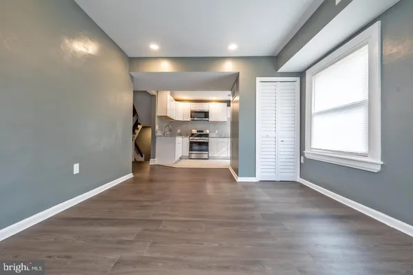 an empty room with wooden floor kitchen view and windows