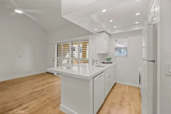 a large white kitchen with a sink and dishwasher a stove top oven with wooden floor
