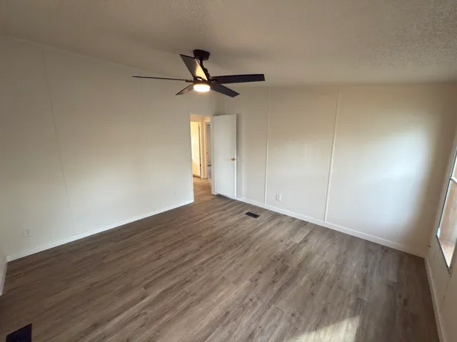 an empty room with wooden floor fan and windows