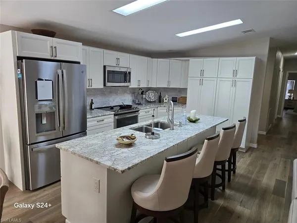 a kitchen with stainless steel appliances granite countertop a dining table chairs refrigerator and microwave