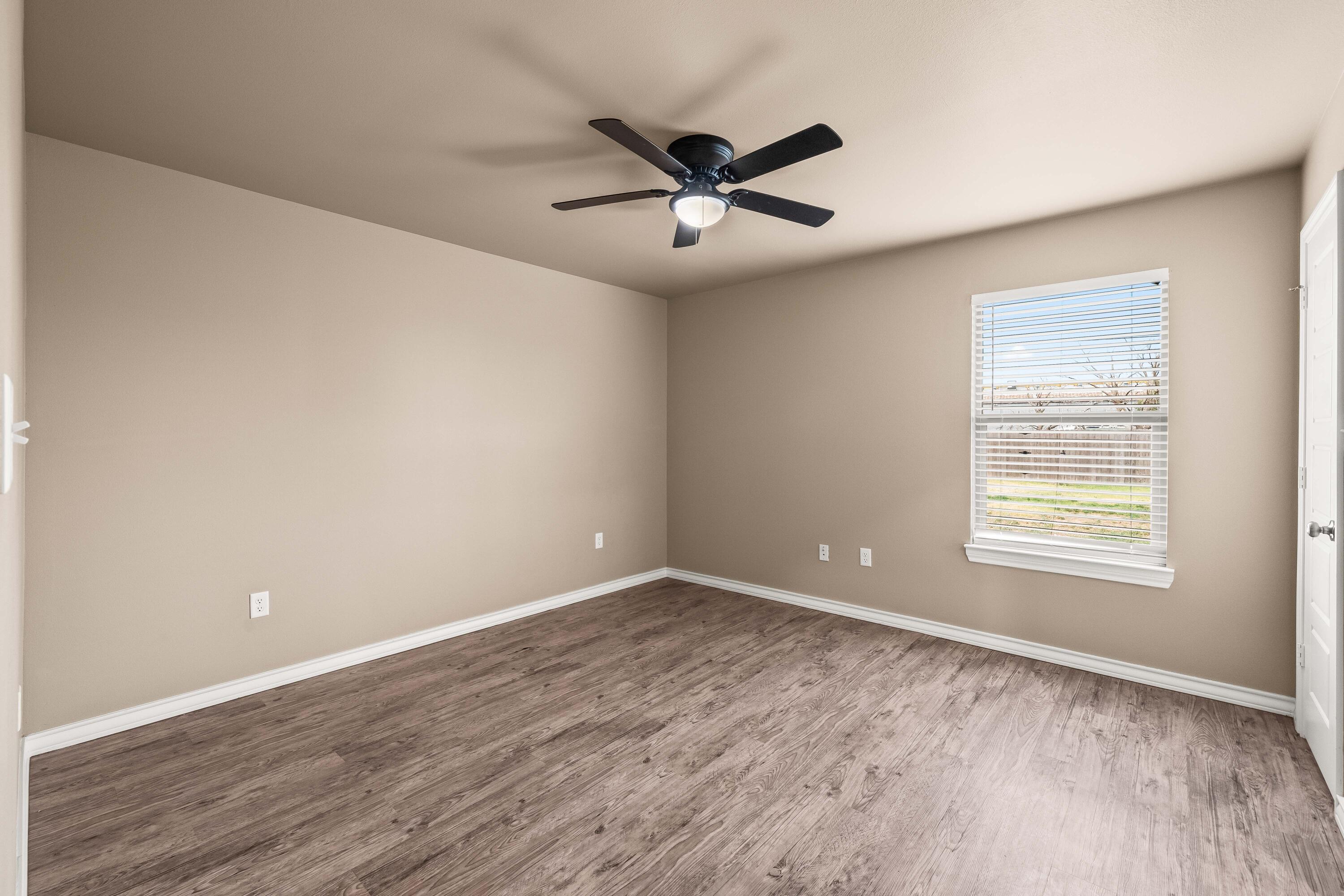 4202 East 64th Street Lubbock, TX 79403 - Photo 11 of 19 an empty room with wooden floor a ceiling fan and windows
