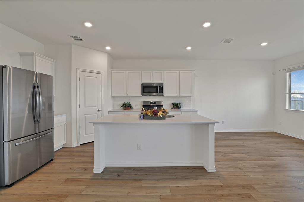 3204 Renaissance Drive Denton, TX 76207 - Photo 9 of 25 Open-concept kitchen featuring an expansive central island, white shaker cabinetry, stainless steel appliances, and wood-finish flooring