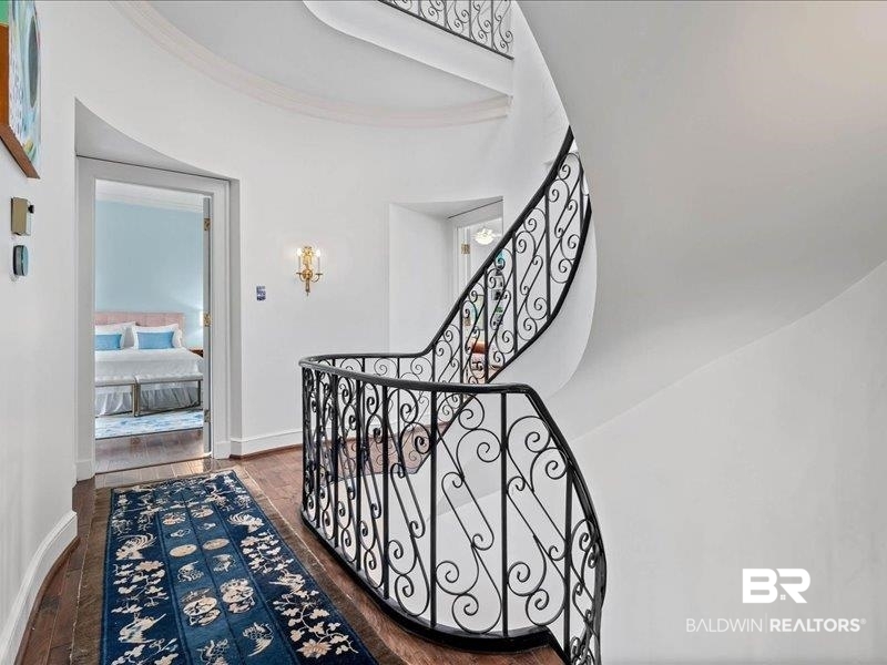109 Eaton Square Mobile, AL 36608 - Photo 11 of 26 Curved staircase with ornate black wrought iron railings, rich wood-finish flooring, and white painted walls