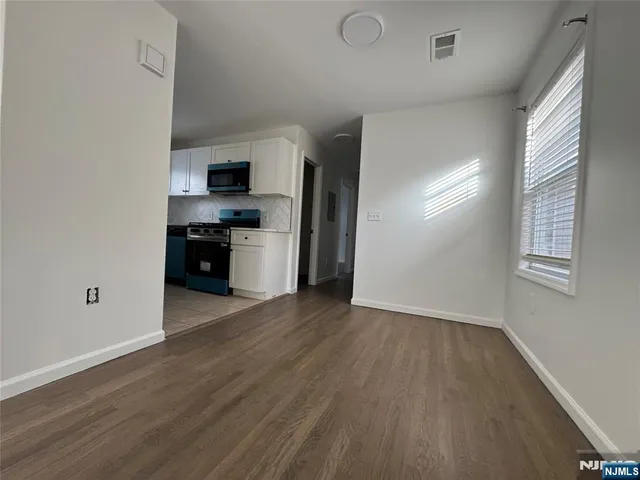 a view of kitchen and empty room with wooden floor
