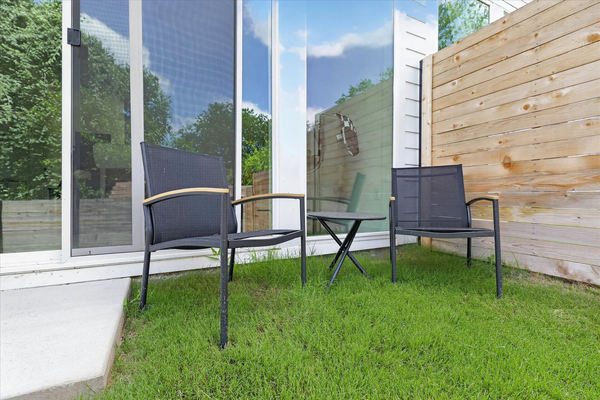 2000 Riverside Farms Road, Unit 8101 Austin, TX 78741 - Photo 36 of 41 This photo shows a cozy outdoor seating area with two chairs and a small table on a grassy patch. It's adjacent to a sliding glass door and enclosed by a wooden fence, offering a private spot to relax.