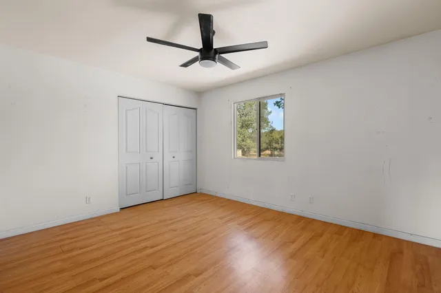 an empty room with wooden floor ceiling fan and windows