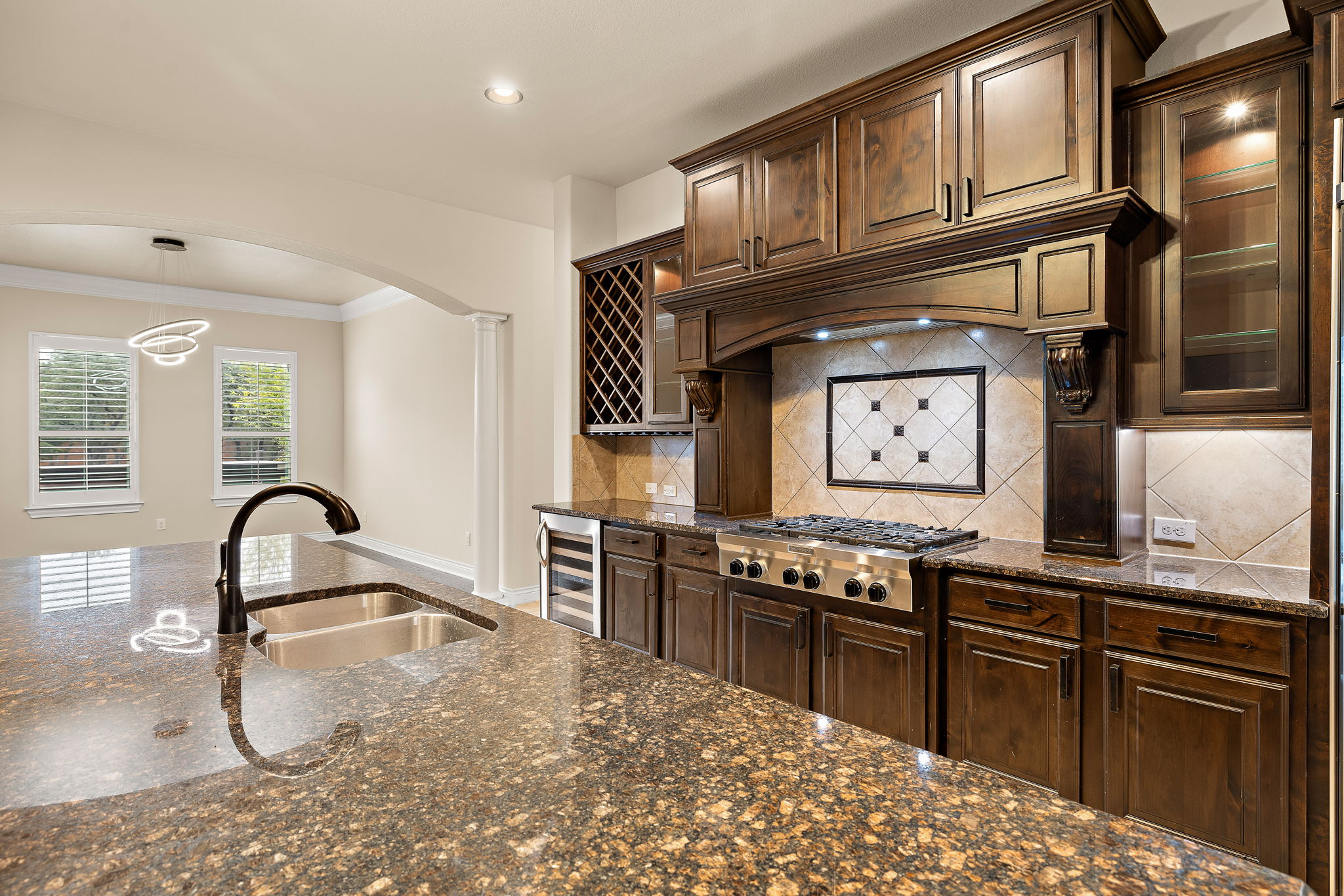 174 Estrella Crossing Georgetown, TX 78628 - Photo 12 of 38 Kitchen featuring dark stone countertops, dark brown cabinetry, arched walkways, decorative light fixtures, and crown molding