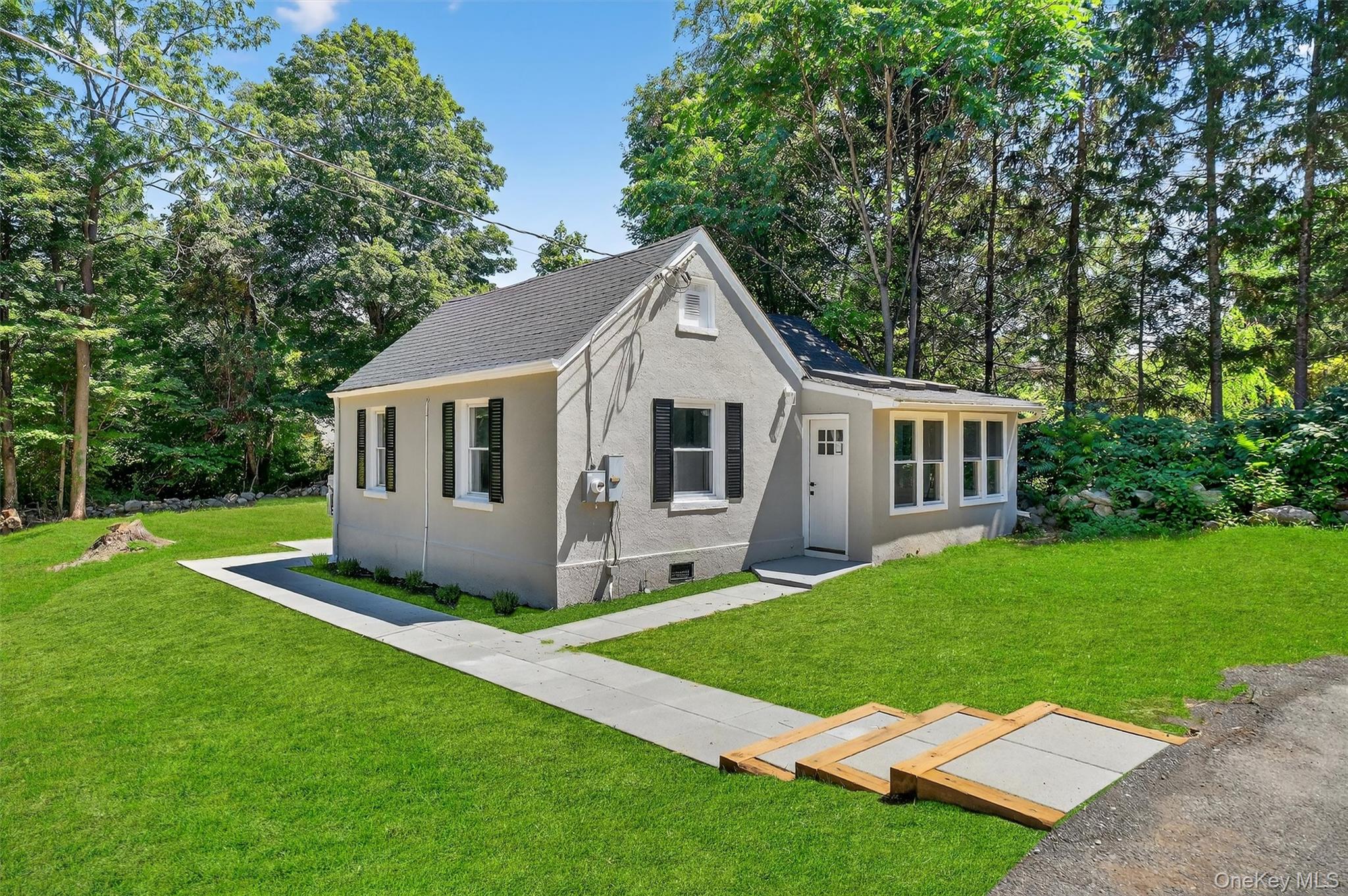 28 Red Brook Road Mahopac, NY 10541 - Photo 1 of 1 Bungalow-style house with a front yard, a shingled roof, stucco siding, and view of wooded area