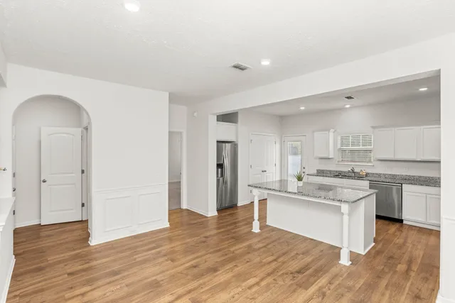 a room with stainless steel appliances granite countertop a dishwasher and a stove with wooden floor