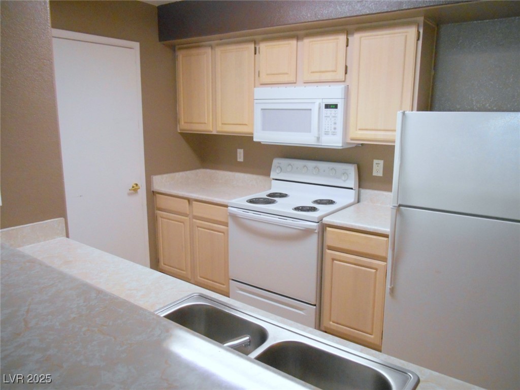 555 East Silverado Ranch Boulevard, Unit 1073 Las Vegas, NV 89183 - Photo 8 of 21 Kitchen featuring white appliances, light brown cabinetry, and light countertops