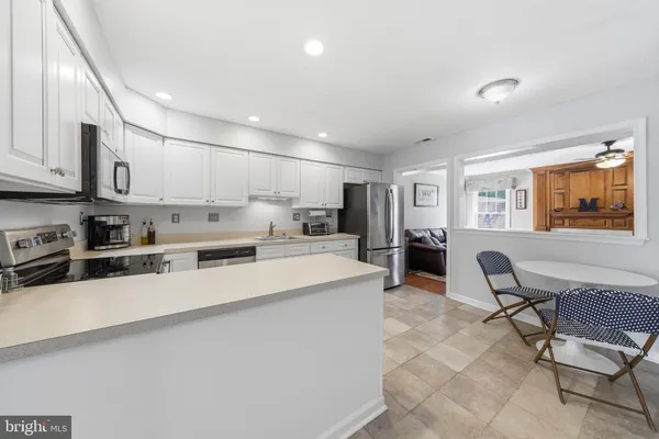 a large white kitchen with stainless steel appliances granite countertop a sink a stove a dining table and chairs with wooden floor