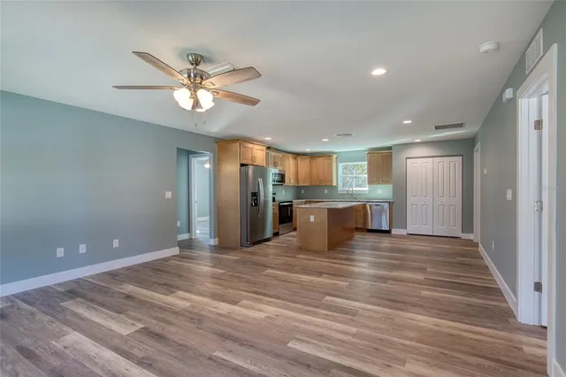 a view of an empty room with kitchen and chandelier fan