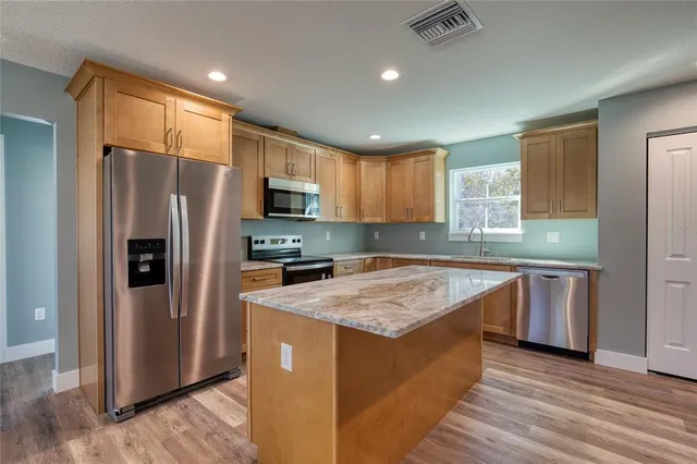 a kitchen with stainless steel appliances granite countertop a refrigerator a sink dishwasher a stove with wooden cabinets and wooden floor