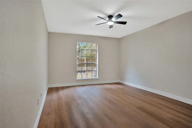an empty room with wooden floor ceiling fan and window