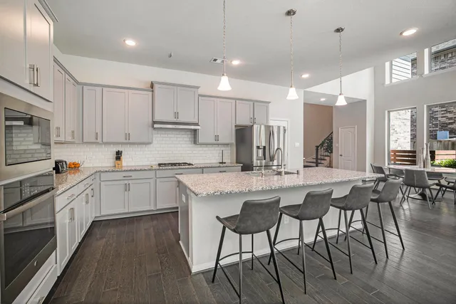 a kitchen with stainless steel appliances granite countertop a stove top oven a sink dishwasher a dining table and chairs with wooden floor