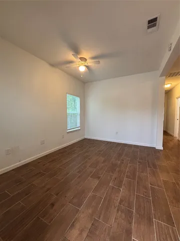 an empty room with wooden floor fan and windows