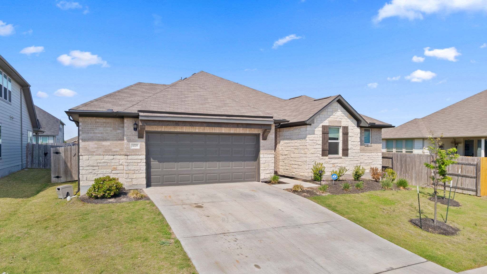4009 Milano River Road Hutto, TX 78634 - Photo 3 of 39 View of front of house with stone siding, an attached garage, driveway, a shingled roof, and a gate