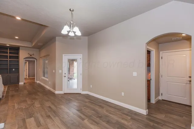 a view of an empty room with wooden floor and chandelier