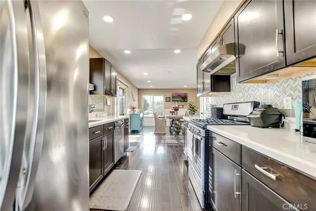 a kitchen with stainless steel appliances granite countertop a refrigerator a sink dishwasher a stove and a sink with wooden floor