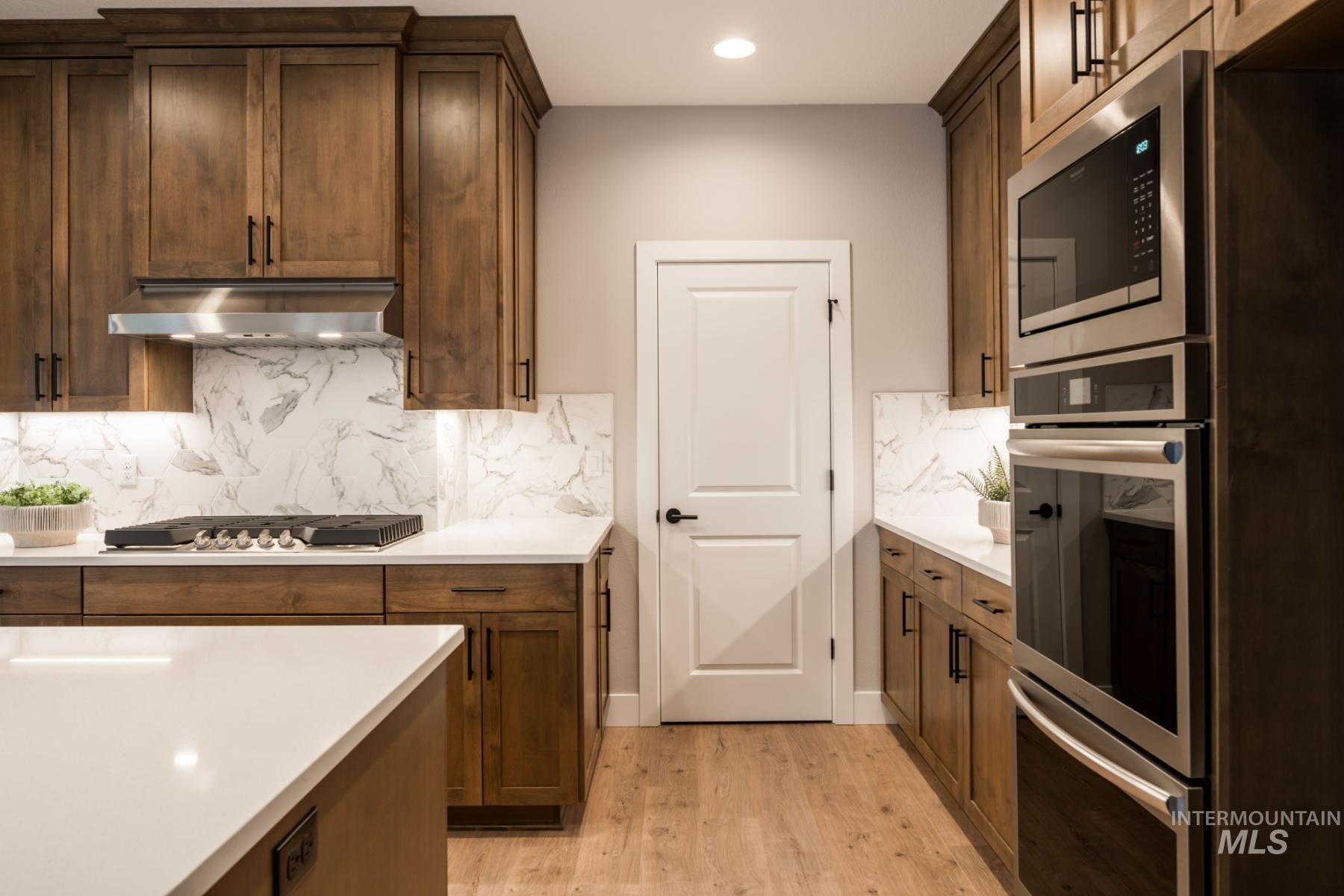1279 West Malbar Street Meridian, ID 83646 - Photo 10 of 23 Kitchen featuring appliances with stainless steel finishes, light wood-style floors, light countertops, tasteful backsplash, and ventilation hood