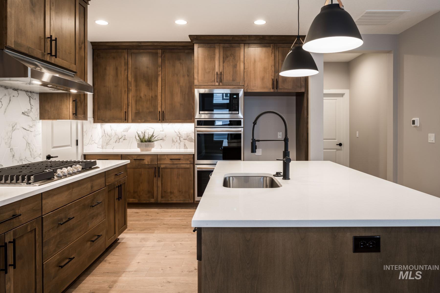 1279 West Malbar Street Meridian, ID 83646 - Photo 7 of 23 Kitchen featuring light countertops, backsplash, recessed lighting, an island with sink, and light wood finished floors