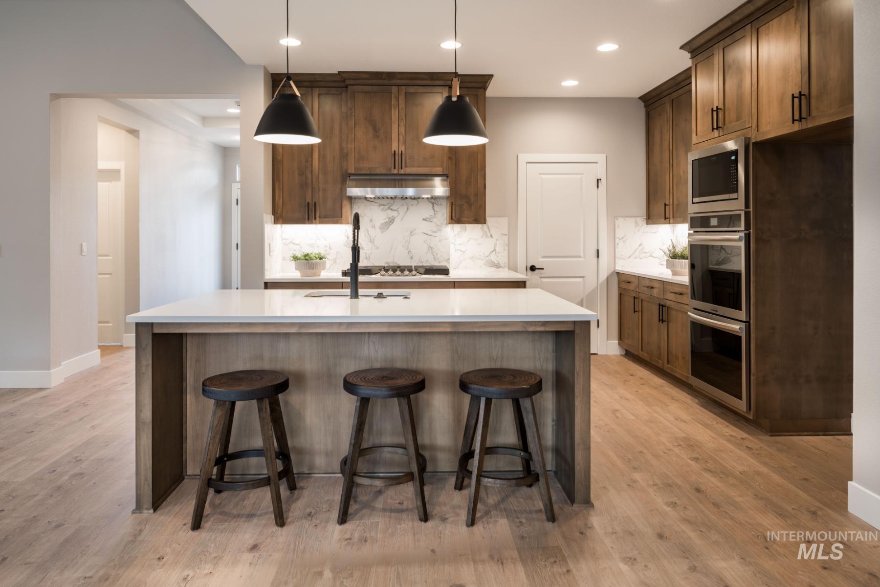 1279 West Malbar Street Meridian, ID 83646 - Photo 9 of 23 Kitchen with decorative backsplash, appliances with stainless steel finishes, an island with sink, light wood-style floors, and light countertops
