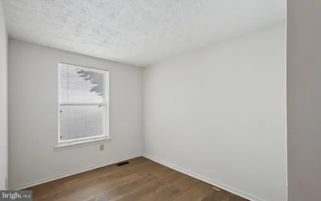 a view of an empty room with a window and hardwood floor