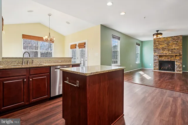 a kitchen with stainless steel appliances kitchen island granite countertop wooden floors wooden cabinets and sink
