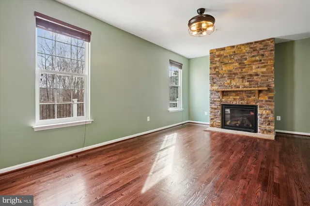 an empty room with wooden floor fireplace and windows