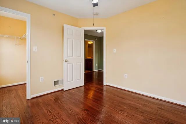 a view of an empty room with wooden floor and a ceiling fan