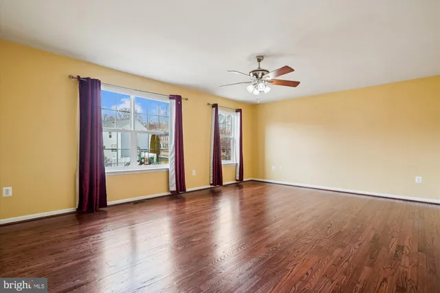 a view of an empty room with wooden floor and a ceiling fan